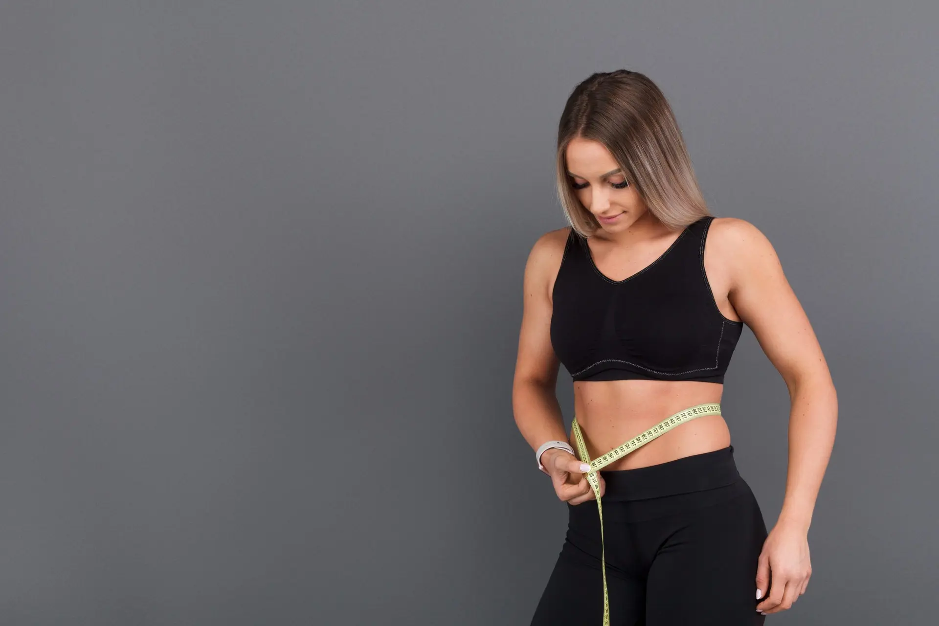 Vrouw in sportkleding meet met een meetlint haar tailleomvang