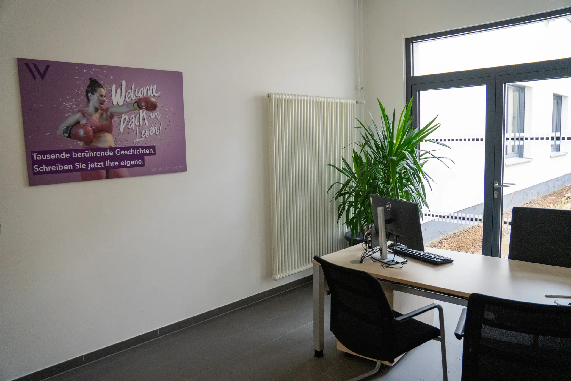 Lichte behandelkamer van de Weight Doctors® Nationalklinik met bureau en Weight Doctors® poster